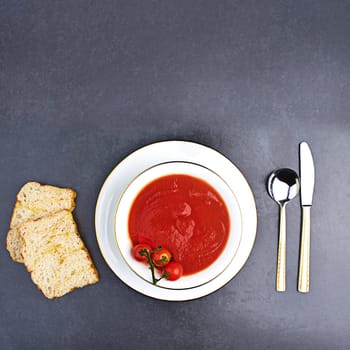 Tomato, soup and bread on menu in restaurant with bowl of healthy food, spoon and knife on table. Dinner, dish or luxury appetizer course in fine dining kitchen with vegetables for nutrition in diet.