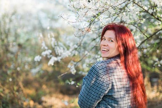Beautiful red-haired woman enjoying smell in a flowering blooming spring garden. Spring blossom.