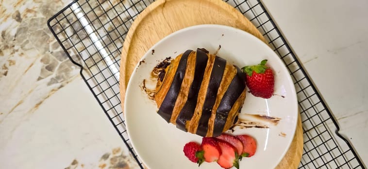 Fresh homemade striped chocolate croissant with chocolate filling on a round white plate, served with fresh strawberry, good cooking ideas