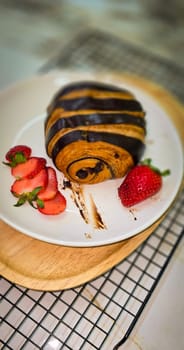 Fresh homemade striped chocolate croissant with chocolate filling on a round white plate, served with fresh strawberry, good cooking ideas