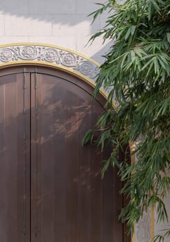 Bangkok, Thailand - Apr 11, 2024 - Front gate of Taiwanese temple, The traditional wooden arched door on white brick wall and bamboo leaves at Fo Guang Shan Thaihua Temple. Taiwanese temple style, Space for text, Selective focus.