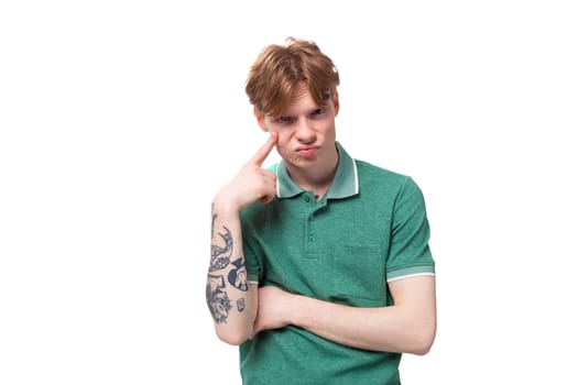 a young man with red hair dressed in a green t-shirt looks thoughtfully ahead.
