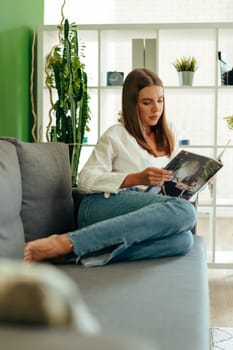 Casual young woman reading magazine on sofa at home portrait