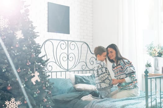 Mother sitting on a bed with her son at home decorated for Christmas, close up