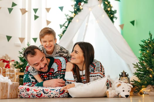 Happy parents play with their little son in a teepee during Christmas holidays, close up