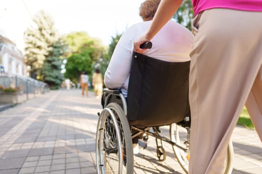 Young female caregiver pushing wheelchair with mature female person with disability across city street