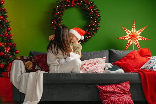 Mother sitting on a sofa with her son in living room decorated for Christmas, close up