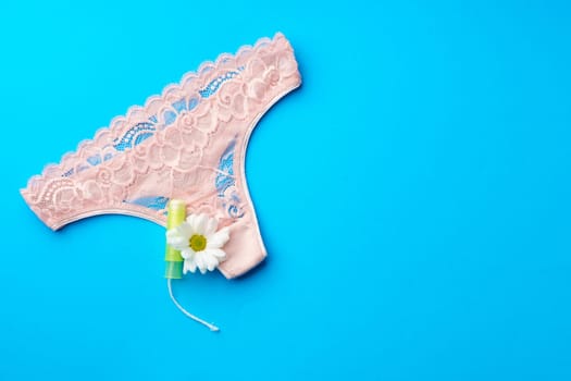 Women's panties with sanitary tampon on color background top view