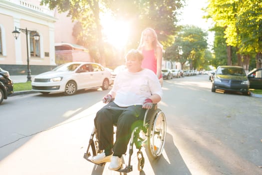 Young female caregiver pushing wheelchair with mature female person with disability across city street