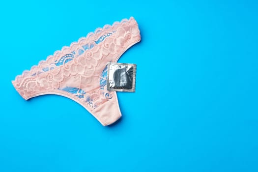 Beautiful women's panties with a condom on a paper background in studio. Safe intimate relationships concept