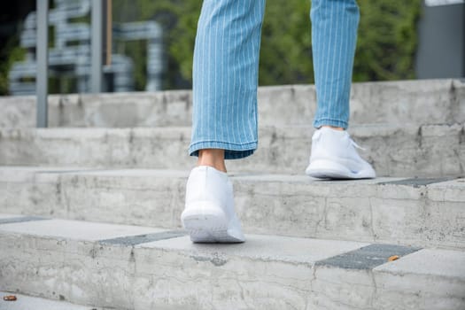 Close-up of a woman's legs in sneakers ascending the city stairway. Every step she takes signifies determination and progress on her journey to success and achievement. step up