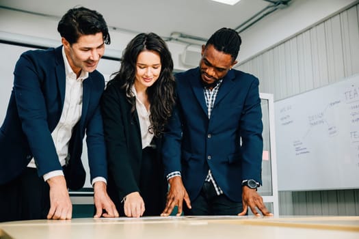 Colleagues at a conference room desk stand, actively planning for business success. Teamwork, diversity, and leadership define this successful meeting.