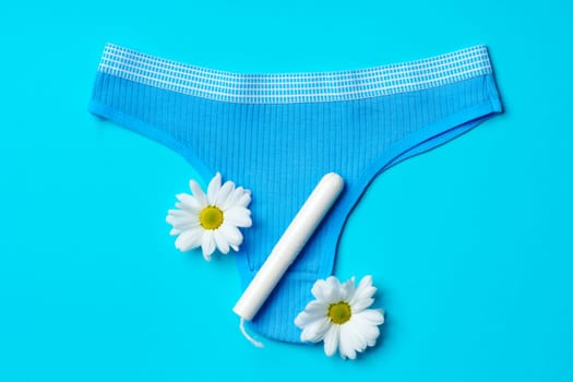 Women's panties with sanitary tampon on color background top view