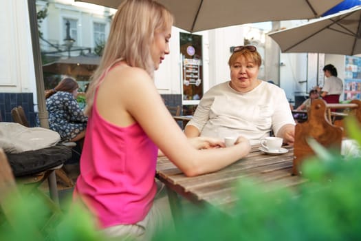Young daughter and her mother in wheelchair sitting at the table in cafe with drinks and having fun, close up