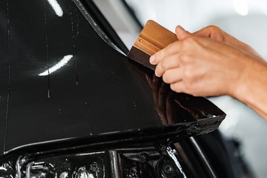 Close up photo of car wrapping specialist putting protective film on a car in detailing service