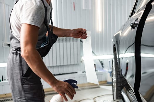 Worker applies car protection film on a car in detailing service, close up