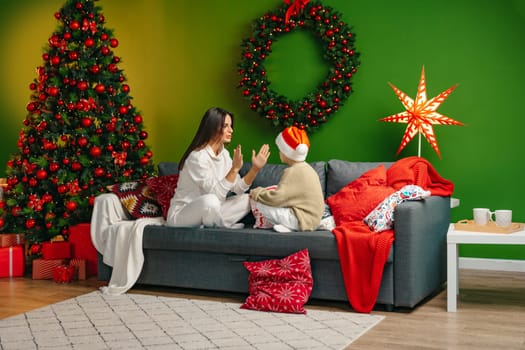 Mother sitting on a sofa with her son in living room decorated for Christmas, close up