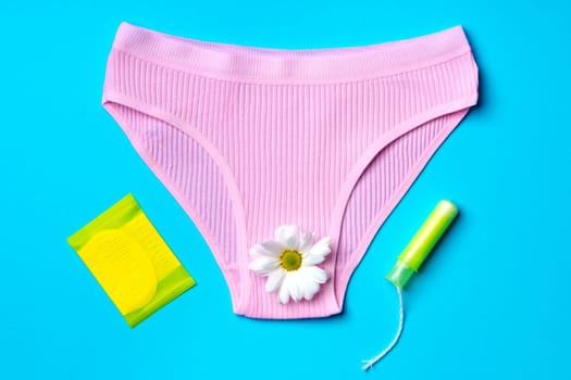 Women's panties with sanitary tampon on color background top view