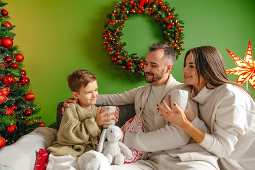 Happy young family sitting on sofa and relaxing at home at Christmas time
