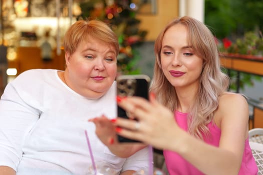 Portrait of mature mother and her daughter making a selfie using smartphone in cafe close up