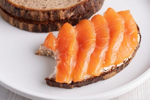 Rye sandwich with salmon and cream cheese on white wooden table.