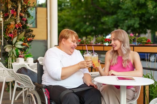 Young daughter and her mother in wheelchair sitting at the table in cafe with drinks and having fun, close up