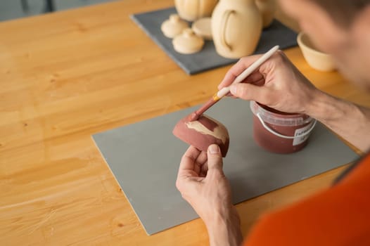 Close-up of a potter's hands with a brush painting ceramic dishes