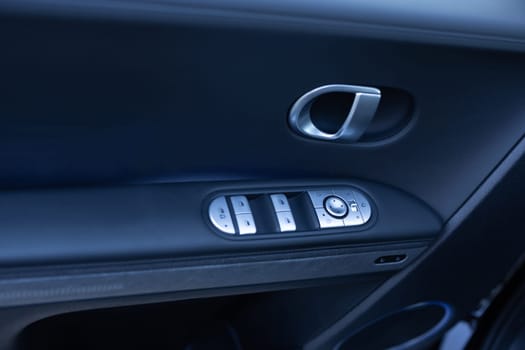 Car window controls. Door handle with power window control. Window control buttons in modern luxury electric car. Car leather interior details of door handle with windows controls and adjustments.