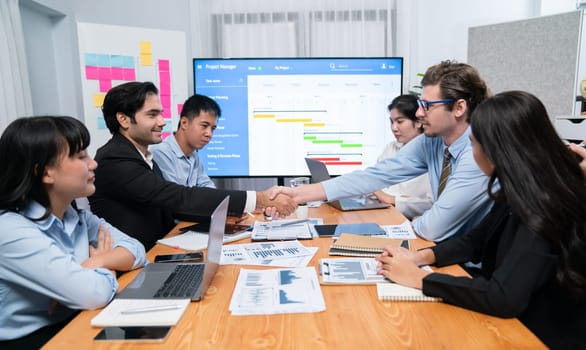 Cheerful meeting room, businesspeople celebrate with handshaking. Successful project was completed before the deadline. Business partnership and collaboration in project management. Habiliment