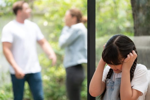 Stressed and unhappy young girl huddle in corner, cover her ears blocking sound of her parent arguing in background. Domestic violence at home and traumatic childhood develop to depression. Synchronos