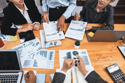 Multiracial analyst team use BI dashboard data to analyze financial report on meeting table. Group of diverse business people utilize data analysis by FIntech for business marketing decision. Concord