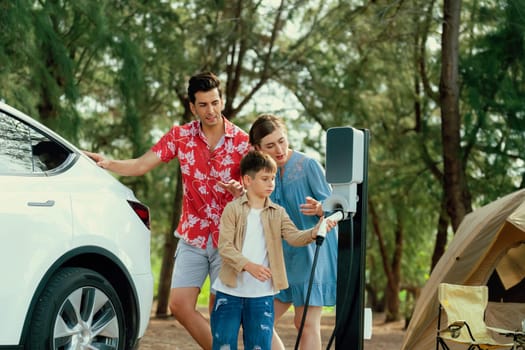 Outdoor adventure and family vacation camping in nature travel by eco friendly car for sustainable future. Lovely family recharge EV car with EV charging station in campsite. Perpetual