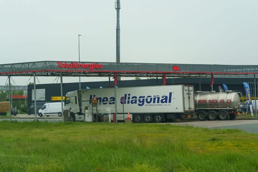 Waregem, Belgium - May 22, 2023: A commercial truck parked in front of a gas station, with a fuel pump nearby and signage for services offered.