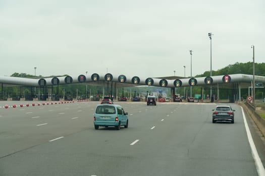 Lille, France - May 23, 2023: Vehicles line up to pay tolls at a modern toll plaza with multiple booths and electronic lane indicators on a cloudy day.