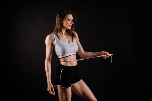 Athletic slim woman measuring her waist by measure tape after diet over dark yellow background