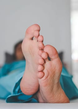 Clean and crossed feet of a young caucasian male patient in disposable pajamas lying on a bed with a blurred background, close-up side view. Body part concept.