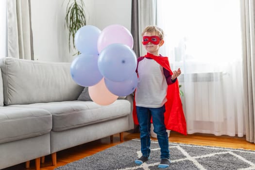 Young boy in superhero costume with balloons indoors.