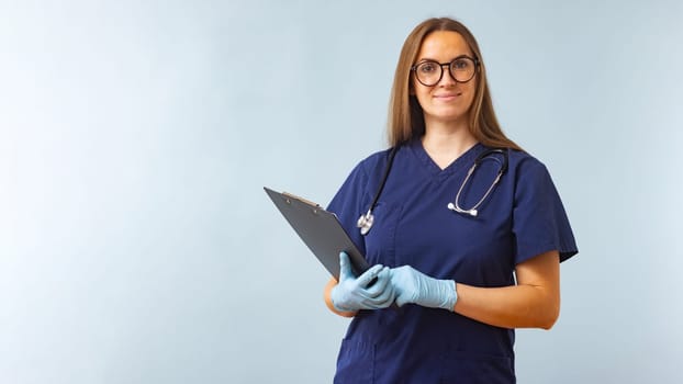 Smiling female healthcare worker in blue scrubs with clipboard. Professional medical staff portrait for healthcare design and poster.