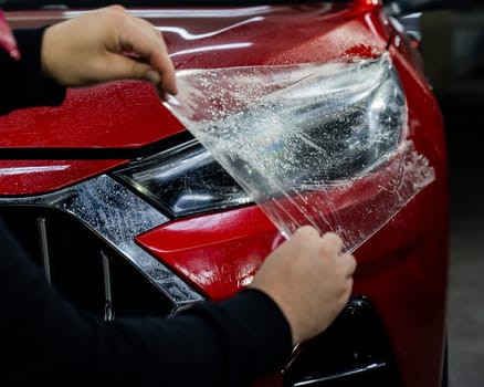 The master applies vinyl film to the headlight of a red car