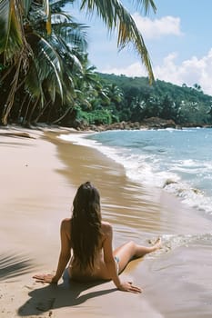 A woman in a bikini relaxes on the sandy beach, gazing at the vast ocean while the sky is filled with fluffy clouds. Nearby, a palm tree sways in the gentle coastal breeze