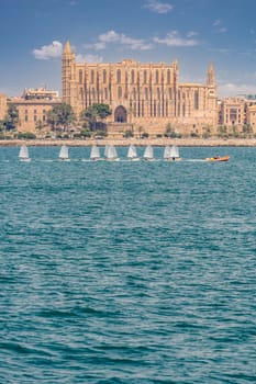 The iconic Majorca Cathedral stands tall behind a line of small sailing boats on a sun-kissed sea