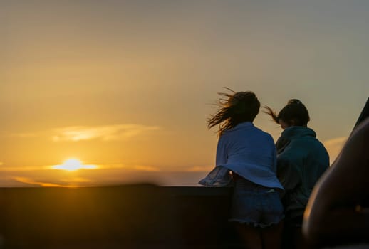 As the day ends, two friends stand against a backdrop of a captivating sunset. Their silhouettes are softly outlined by the radiant glow of the descending sun.