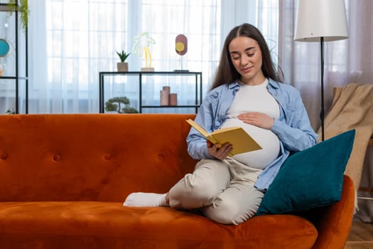 Pregnant Caucasian woman lady reading book feeling relax on cozy sofa couch at home. Future mother beautiful female read advice child care guide prepare prenatal. Relaxation and pregnancy concept.