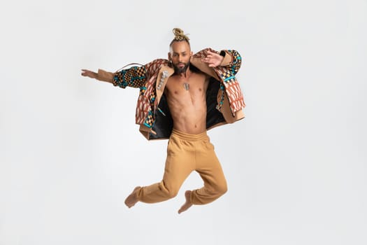 Full length gay man jumping wearing stylish clothing dancing isolated on white. Brazilian homosexual male posing in photo studio. Bearded afro-american gay man cut out on white.