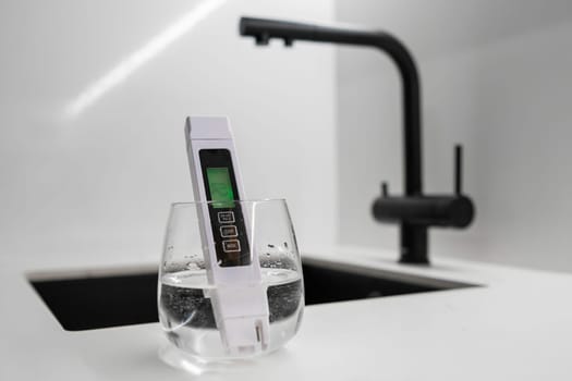 TDS meter immersed into the water in glass shows that the water is clean in modern kitchen. Clean tap water concept.