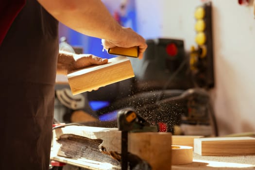 Craftsperson at workbench using manual sandpaper to sander lumber block, assembling furniture in woodworking shop. Carpenter smoothing piece of wood, enjoying diy hobby, close up