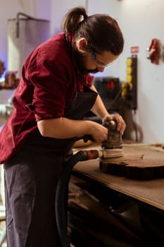 Craftsperson at work using orbital sander with fine sandpaper on lumber to achieve smooth finish. Woodworking expert in carpentry shop uses angle grinder on wood for professional results