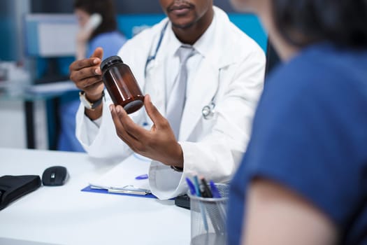 Close-up shot of an African American doctor describing the diagnosis and course of treatment of a caucasian patient while holding a bottle of medication. A woman receiving medical advice.