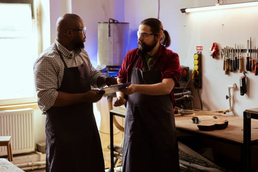 Craftsperson and colleague looking over technical schematics to make commissioned wooden object. Manufacturer and coworker looking at blueprints to execute furniture assembling woodworking project