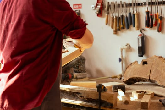 Manufacturer using sandpaper for smoothing wooden surface before polishing it, ensuring adequate finish. Woodworking professional using sanding sheets to fix damages suffered by lumber block